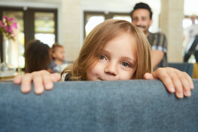 young child looking over back of blue couch