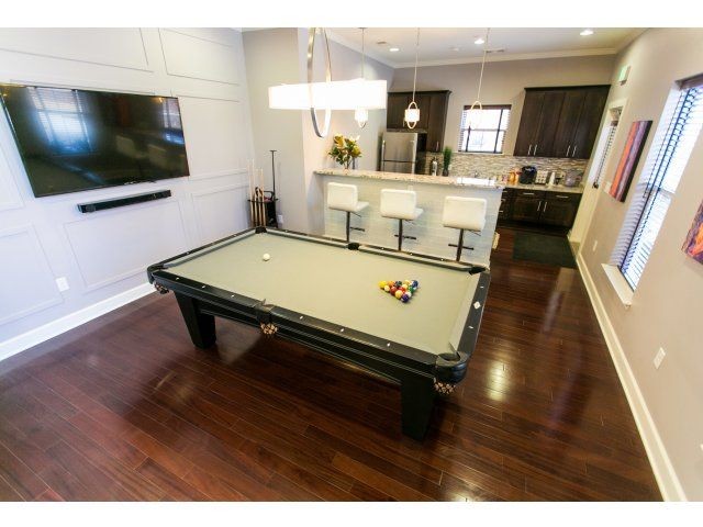 Pool table on hardwood floor near kitchen area, flatscreen TV on the wall