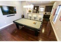 Pool table on hardwood floor near kitchen area, flatscreen TV on the wall