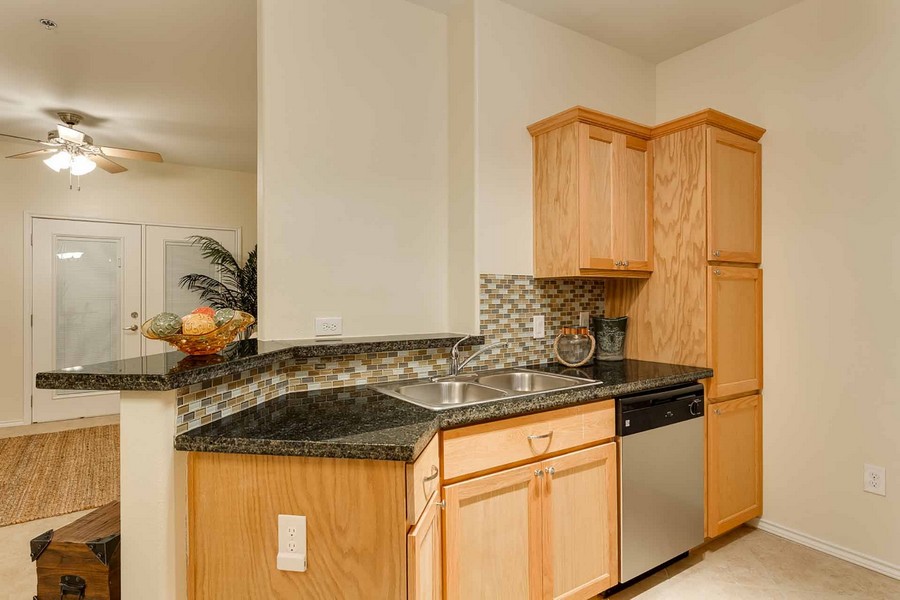 Apartment kitchen with light wood cabinetry, dual basin sink, and granite countertops