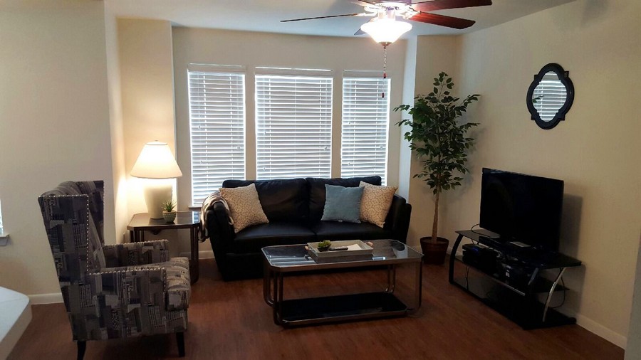 Apartment living room with couches and large windows covered with blinds 